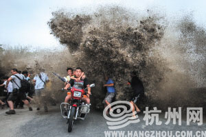 下沙七格江边，一位男子不戴头盔，还带着孩子家人，骑着摩托车试图穿过潮水。但还是被潮水打翻，压倒了两个摄影爱好者。