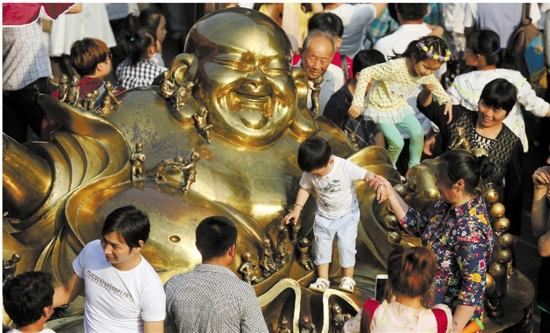5月1日的杭州河坊街，几位大人将孩子抱上弥勒佛。