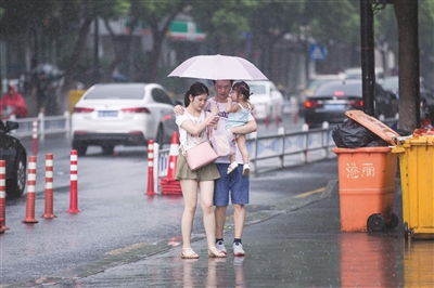 昨日午后，突然下了雷阵雨。一家三口挤在伞下。记者 许康平 摄