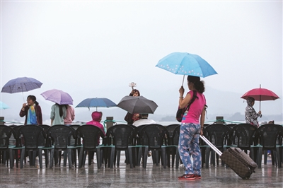 昨天下午，游客撑着伞在雨中等待观看西湖音乐喷泉。 