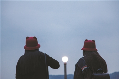 两位戴着相同帽子的女生，在西湖边等待着夜色的降临。