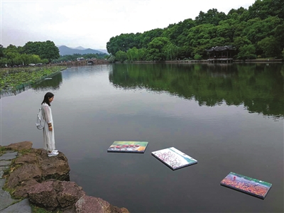 一个女孩站在西湖边，观看“写给杭州的诗”水上摄影展。 