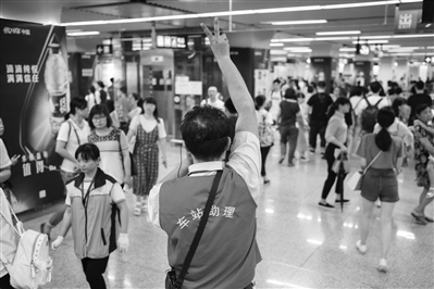 地铁凤起路站，一位车站助理面对走出1号线的乘客比出两根手指，示意换乘2号线的方向。